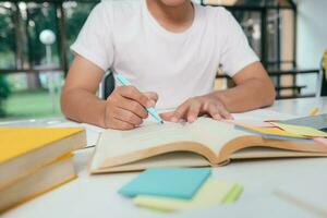 cerca arriba joven asiático masculino estudiante es preparando a leyendo un libros para exámenes a universidad. foto