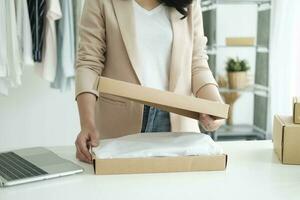 Asian female clothes shop owner folding a t-shirt and packing in a cardboard parcel box. photo