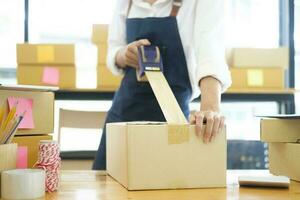 Asian female clothes shop owner folding a t-shirt and packing in a cardboard parcel box. photo