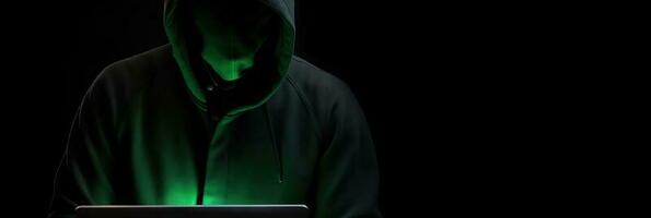 Hacker without face in a hood holds a laptop. on a dark background. Banner for cyber security.  Internet web hack technology. Digital laptop in hacker man hand isolated on black. photo