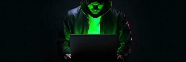 Hacker without face in a hood holds a laptop. on a dark background. Banner for cyber security.  Internet web hack technology. Digital laptop in hacker man hand isolated on black. photo