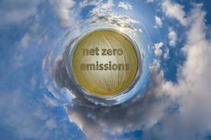 net zero emissions text concept image against green tiny planet in blue sky with beautiful clouds photo