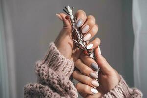 Women's hands with a beautiful matte oval manicure in a warm knitted sweater. Hands are holding a winter branch. Varnish beige nails with gel polish, shellac. Copy space. photo