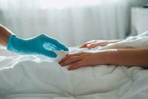 The child lies in bed, a doctor in medical gloves comes up to him and puts a pulse oximeter on his finger to measure the oxygen saturation. Asthma treatment. photo