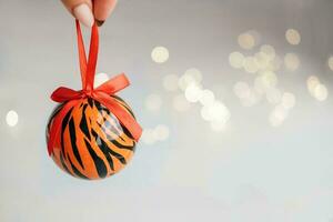 Christmas ball painted as tiger stripes spins on blurred christmas garland. background.  2022 is a year of the Tiger. Happy New Year . Symbol of year lunar chinese calendar tiger on Christmas  bal photo