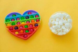 Use the popular pop it toy as a chocolate mold. White chocolate, colorful candies and popit heart-shaped silicone mold on yellow background. DIY concept. Step-by-step photo instructions. Step 1.