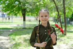 un niña en un especial uniforme con un S t. Jorge cinta sostiene Tres claveles en su manos. fiesta victoria día mayo 9º foto