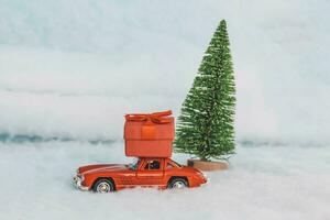 Krasnodar, Russia - December 10, 2019 Red toy car with a gift on the roof, rides in the snow. Delivery of gifts. Copy space. Christmas . New year. photo