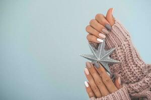 Women is hand with a beautiful matte oval manicure. Female hands are holding a New Year is a star. Varnish beige nails with gel polish, shellac. Copy space. Christmas manicure. photo