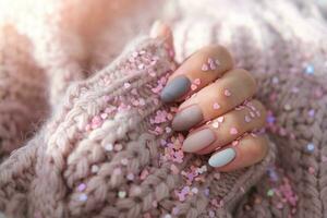 Women's hands with a beautiful matte oval manicure in a warm purple knitted sweater and heart shaped sequins. Winter trend, polish beige nails with gel polish, shellac. Copy space. photo