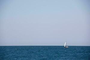 pequeño navegación yate con grande blanco paño en el abierto mar en el horizonte foto