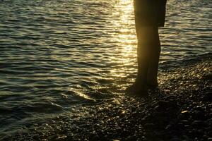 man walking alone on the pebble beach in the sunset photo