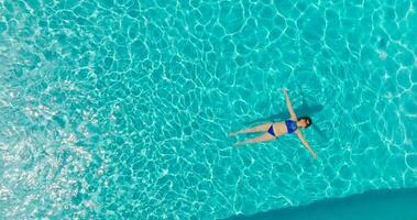 parte superior abajo ver de un mujer en azul traje de baño acostado en su espalda en el piscina. video