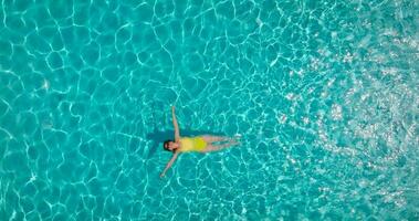 Top down view of a woman in yellow swimsuit lying on her back in the pool. video