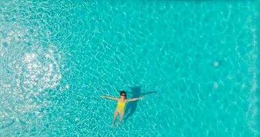 Top down view of a woman in yellow swimsuit lying on her back in the pool. video