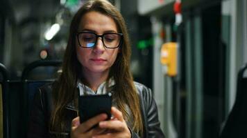 público transporte a noche. mujer en lentes en tranvía utilizando teléfono inteligente video