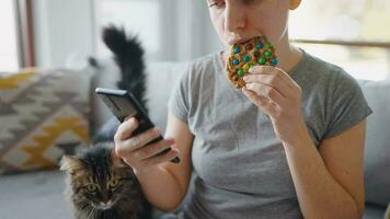 Woman eating colourful chip cookie and using smartphone in the same time video