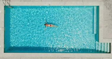 superiore giù Visualizza di un' donna nel rosso costume da bagno dire bugie su sua indietro nel il piscina. video