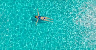 parte superior abajo ver de un mujer en azul traje de baño acostado en su espalda en el piscina. video