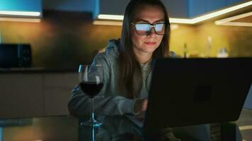 Woman is sitting in the kitchen and working on a laptop at night video