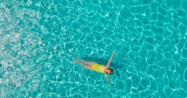 Top down view of a woman in yellow swimsuit lying on her back in the pool. video