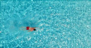 aéreo ver de un hombre en rojo pantalones cortos nadando en el piscina, lento movimiento. video