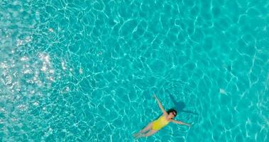 Top down view of a woman in an yellow swimsuit lying on her back in the pool. video