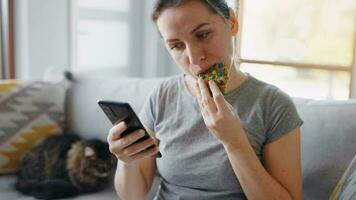 mulher comendo colorida lasca bolacha e usando Smartphone dentro a mesmo Tempo video