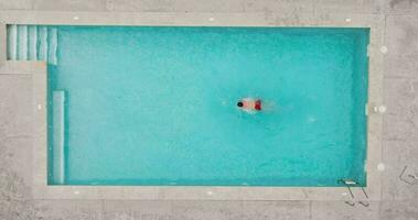 aéreo ver de un hombre en rojo pantalones cortos nadando en el piscina. video