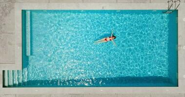 Top down view of a woman in red swimsuit lying on her back in the pool. video