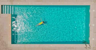 superiore giù Visualizza di un' donna nel un giallo costume da bagno dire bugie su sua indietro nel il piscina. video