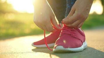 Woman tying shoelaces while jogging or walking at sunset. Slow motion video