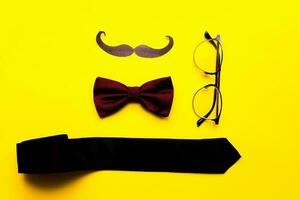 Flat lay mustache, glasses, bow tie and necktie on a yellow background. happy fathers day photo