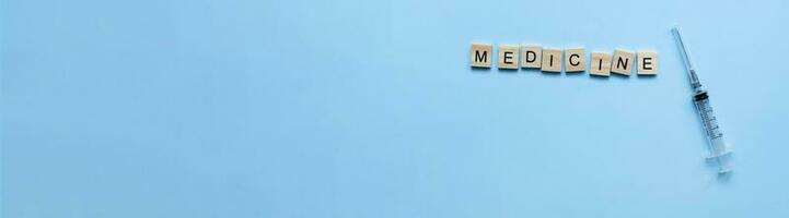 Banner The word medicine from wooden letters on a blue background. Syringe, vaccine, injection, inoculation photo