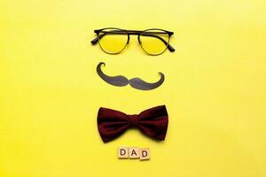 Happy fathers day. Flat lay glasses, mustache, bow tie on yellow background photo