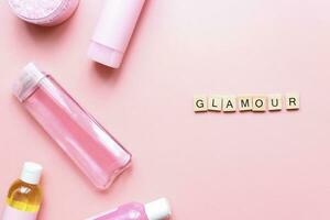 Flat lay word glamor from wooden letters on pink background. Bottles mockup. spa jars photo