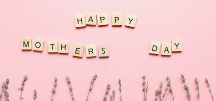 Happy Mothers Day banner made of wooden letters on a pink background with flowers. Mothers day card. photo