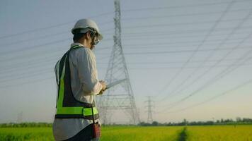 Electrical engineer wearing uniform holding tablet working near high voltage pylon video