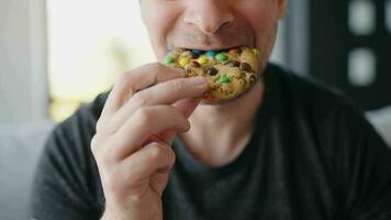 Hungry man biting and chewing colourful chip cookie close-up video