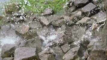 Drops of water from a waterfall falling on gray stones and flying in different directions. video