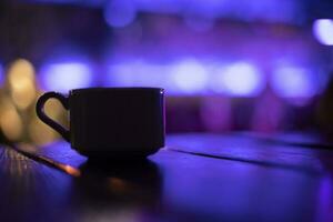 Cup on table in purple. Silhouette of cup in dark room. Mug with drink. photo