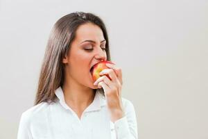 un mujer con un blanco camisa comiendo un manzana foto