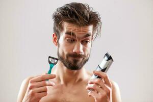 An indecisive man holding a razor and an electric shaver photo