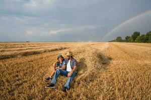 padre y hijo son en pie en su trigo campo después un exitoso cosecha. foto