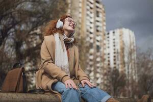 contento joven mujer con pecas y Rizado jengibre pelo escuchando a música al aire libre foto