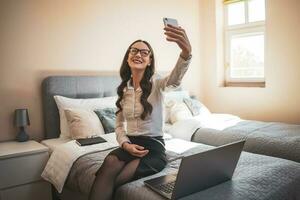 A woman taking a selfie and working in her room on a laptop photo