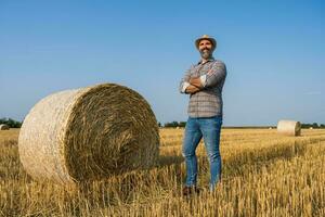 A farmer is standing beside bales of hay photo