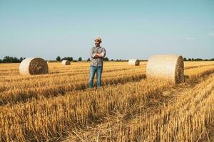 A farmer is standing beside bales of hay photo