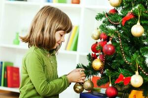 un pequeño niña pone un ornamento en el Navidad árbol foto