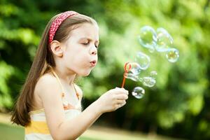 un joven niña haciendo jabón burbujas foto
